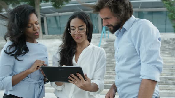 Three Colleagues Standing Outside Watching at Tablet’s Screen