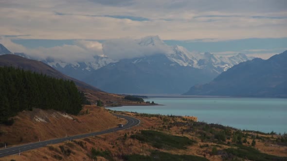 Cars driving along the coast of glacial Lake Pukaki, towards the Southern Alps and Mount Cook in New