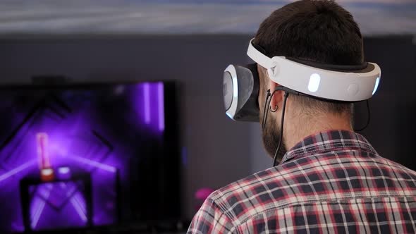 A Young Man Wearing Virtual Reality Glasses Plays VR Games in the Game Room