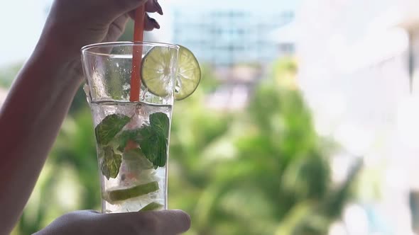 Woman Hand Stirs Frozen Mojito Cocktail in Tall Glass