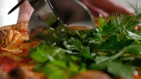 baker cuts fresh hot pizza with aromatic herbs with a round knife before serving