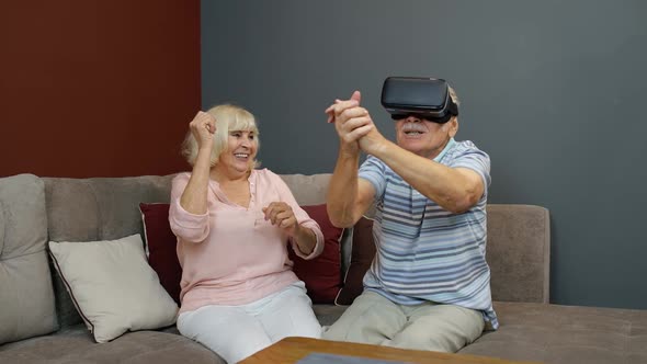 Senior Man Playing Game in Virtual Reality Headset Glasses, Woman Laughing with Him Action at Home