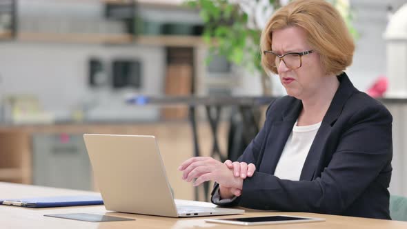 Old Businesswoman with Laptop Having Wrist Pain in Office 