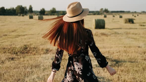 Playful Redhaired Girl Walks Among Windy Straw Field. Girl In Hat Enjoying Weekend. Happy Ginger