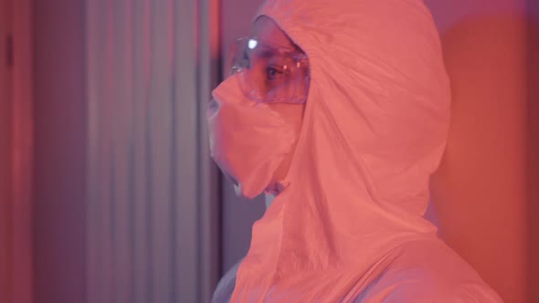 Side View of Exhausted Depressed Medical Worker Moving Down the Wall in Room with Red Lighting