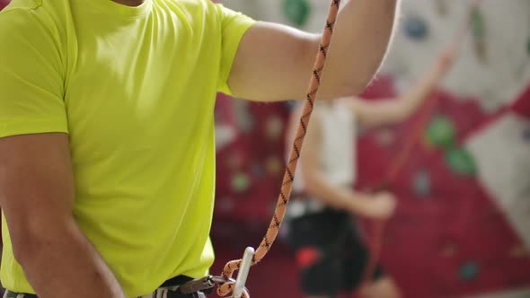 Closeup of Climber Man Belaying Another Climber Against a Wall with Hooks