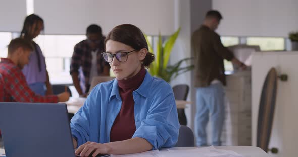 Casual Businesswoman Sitting at Desk in Office Working on Laptop