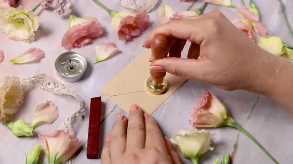 Hands sealing melted wax on an envelope near pink flowers