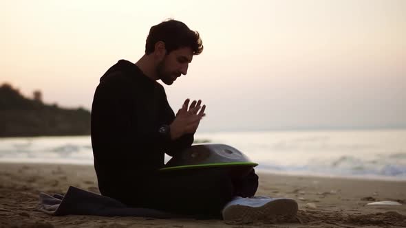 The Man in Black Casual Playing Hang Sitting on the Beach in Front the Sea Alone