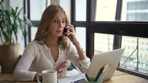 Businesswoman Having Mobile Call in Front of Laptop Screen at Table in Home Office