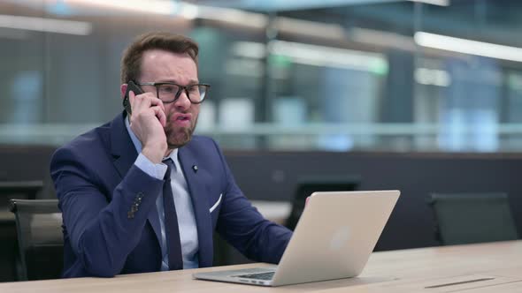 Angry Middle Aged Businessman with Laptop Talking on Phone