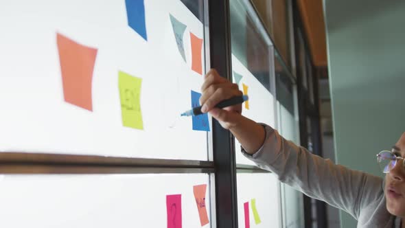 Happy biracial female creative businesswoman writing on memo notes, brainstorming in office