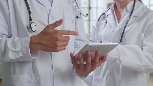 Doctor's Office: Asian Physician Talks With Professional Nurse, Using Tablet Computer