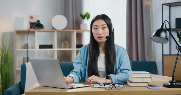 Asian Girl in Headphones with Mic which Poses on Camera During Video Meeting with Mentor or Tutor