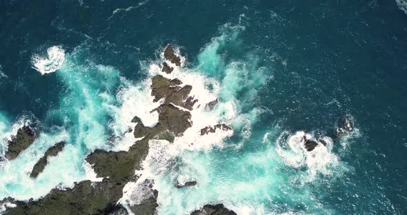 Aerial top down shot of coral rocks hitting by sea waves during sunny day in Yogyakarta,Indonesia