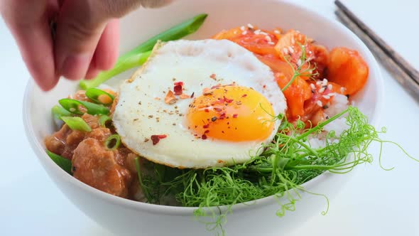 Bibimbap - meat, rice, kimchi, egg and sprouts in white bowl.