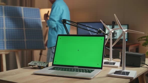 Green Screen Laptop With Turbine On The Table While Man Walks Into The Office To Look At Solar Cell
