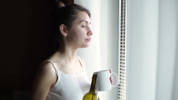 the girl goes to the window with a cup of coffee and pours red wine into it