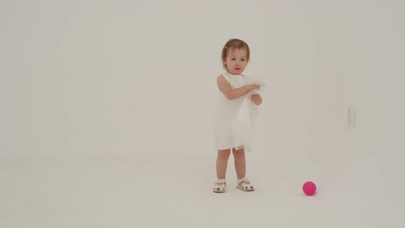 Little Girl in Dress is Playing on the White Carpet