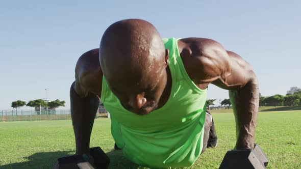 Tired african american man exercising outdoors doing press ups and lifting dumbbells