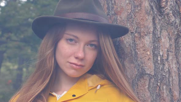 Portrait of Red Haired Tourist Girl with Yellow Raincoat and Hat Looks at Camera Through the Smoke