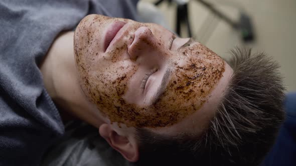 Close Beautician's Hands Massaging Man's Face with Coffee Scrub in a Salon