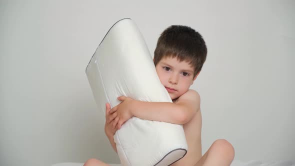 A 5Yearold Boy Hugs His Favorite Orthopedic Pillow While Sitting on the Bed