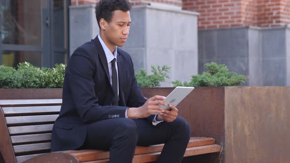 African Businessman Using Tablet , Sitting on Bench