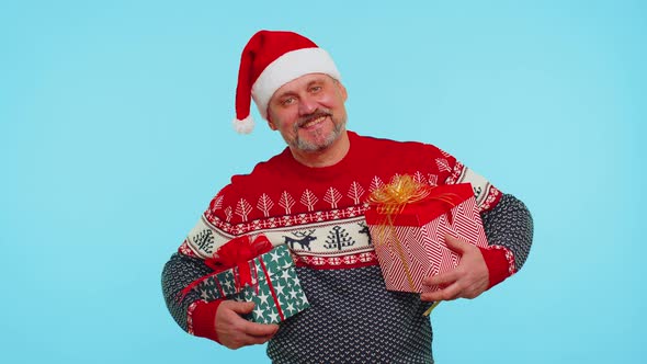 Cheerful Man in Santa Sweater Presenting Two Christmas Gift Boxes Stretches Out His Hands to Camera