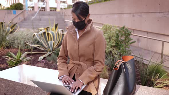 Mixed ethnicity business woman wearing a face mask works on her laptop