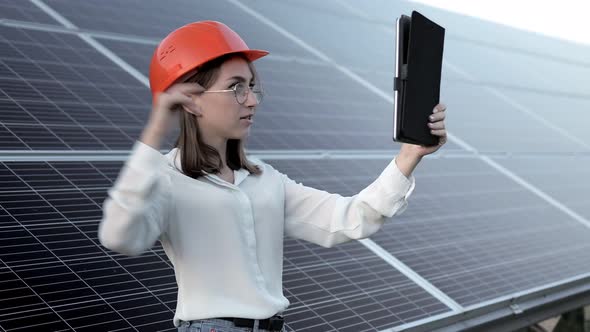 Beautiful young engineer standing near solar panels outdoors, Green Energy Concept.