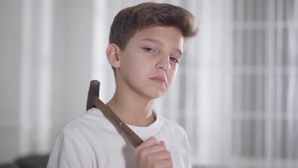 Close-up Portrait of Serious Caucasian Brunette Boy in White T-shirt Holding Hammer on Shoulder and