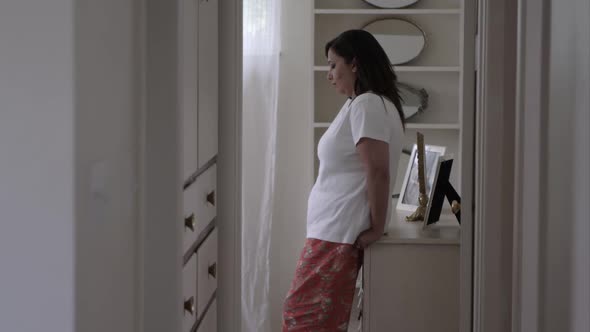 Woman in her bedroom leaning against her dresser.