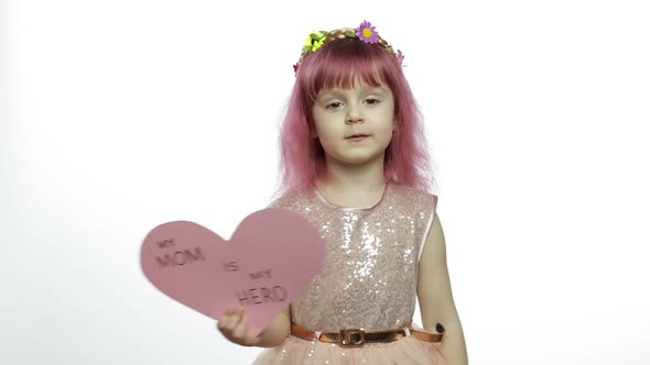 Child Girl Princess Holds Pink Paper Heart with Text About Mother. Mother's Day