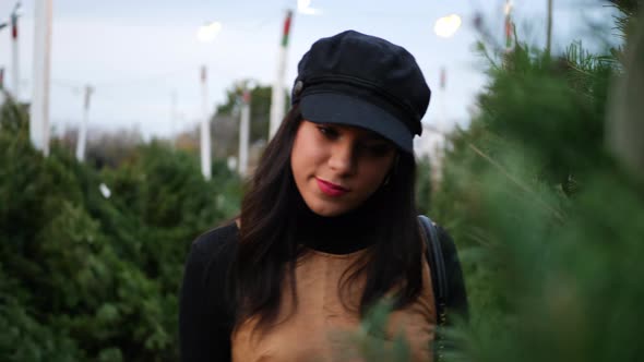 A hispanic woman shopping for a seasonal holiday Christmas tree on a lot with many species of festiv