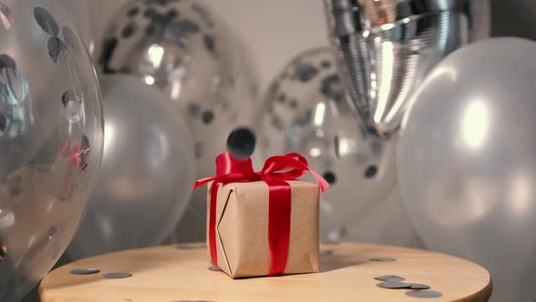 Gift Box with a Red Ribbon and a Bow on the Background of Balloons Silver Confetti Falling From