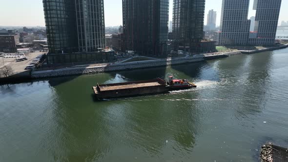 An aerial view of a barge sailing down Newtown Creek with new high-rise apartment buildings in Brook