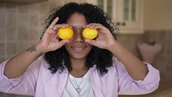 Front View Happy Joyful African American Woman Grimacing Covering Eyes with Lemons Looking at Camera