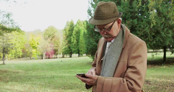 Elegant Senior Man Typing on Smartphone in Beautiful Sunny Park