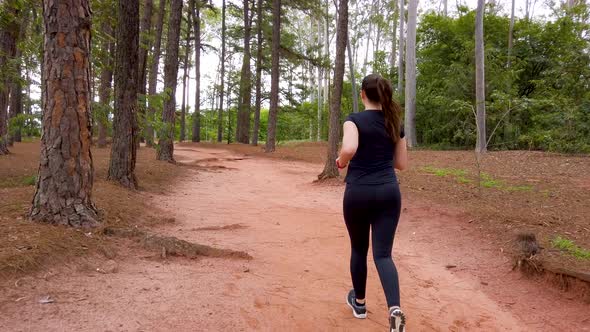 Girl jogging on a dirt trail between trees, camera following the subject from behind.