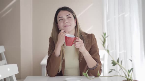 Portrait of Dreamy Thoughtful Beautiful Woman Smelling Delicious Coffee or Tea in Cup and Smiling