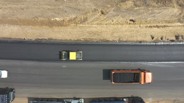 Aerial Shot of Roller Laying New Asphalt Layer and Trucks Standing at Roadside