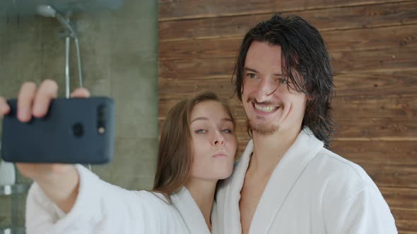 Man and Woman in Bathrobes Having Fun Taking Selfie in Hotel Bathroom