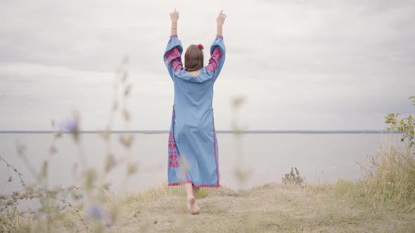 Back View of Attractive Barefoot Young Brunette Girl with Red Flower in Hair and Beautiful Blue Long