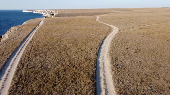 Bird'seye View of a Dusty Gravel Road in a Steppe Area in a Field Near a Cliff Rocky Seashore