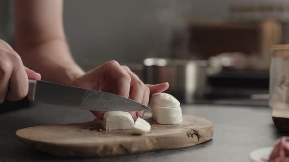 Slow Motion Man Slicing Mozzarella on Olive Board