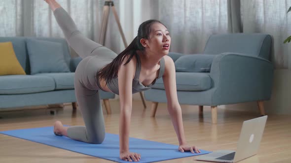 Female Exercising, Stretching And Practicing Yoga At Home With Online Coach Via Laptop Computer