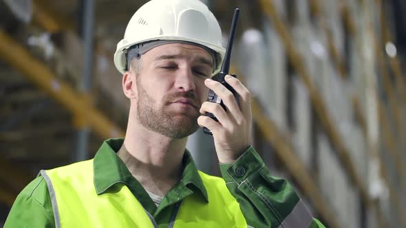 Young American Man Is Talking on Walkie-talkie While Standing in Industrial Warehouse