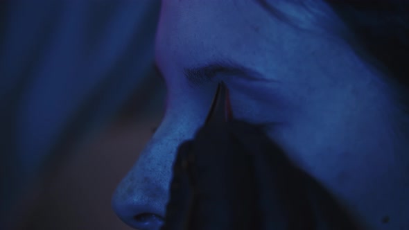 A Man Makeup Artist Plucks Hairs of His Female Client's Brows in Dark Blue Lighting