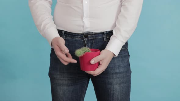 A Man in a White Shirt and Jeans Holds a Red Cactus Pot Against the Background of His Groin
